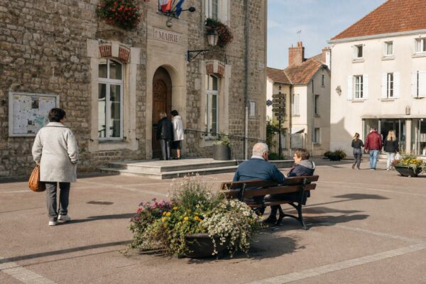 Place de ville française près d’une mairie, passants anonymes et ambiance civique en lumière de fin d’après-midi.