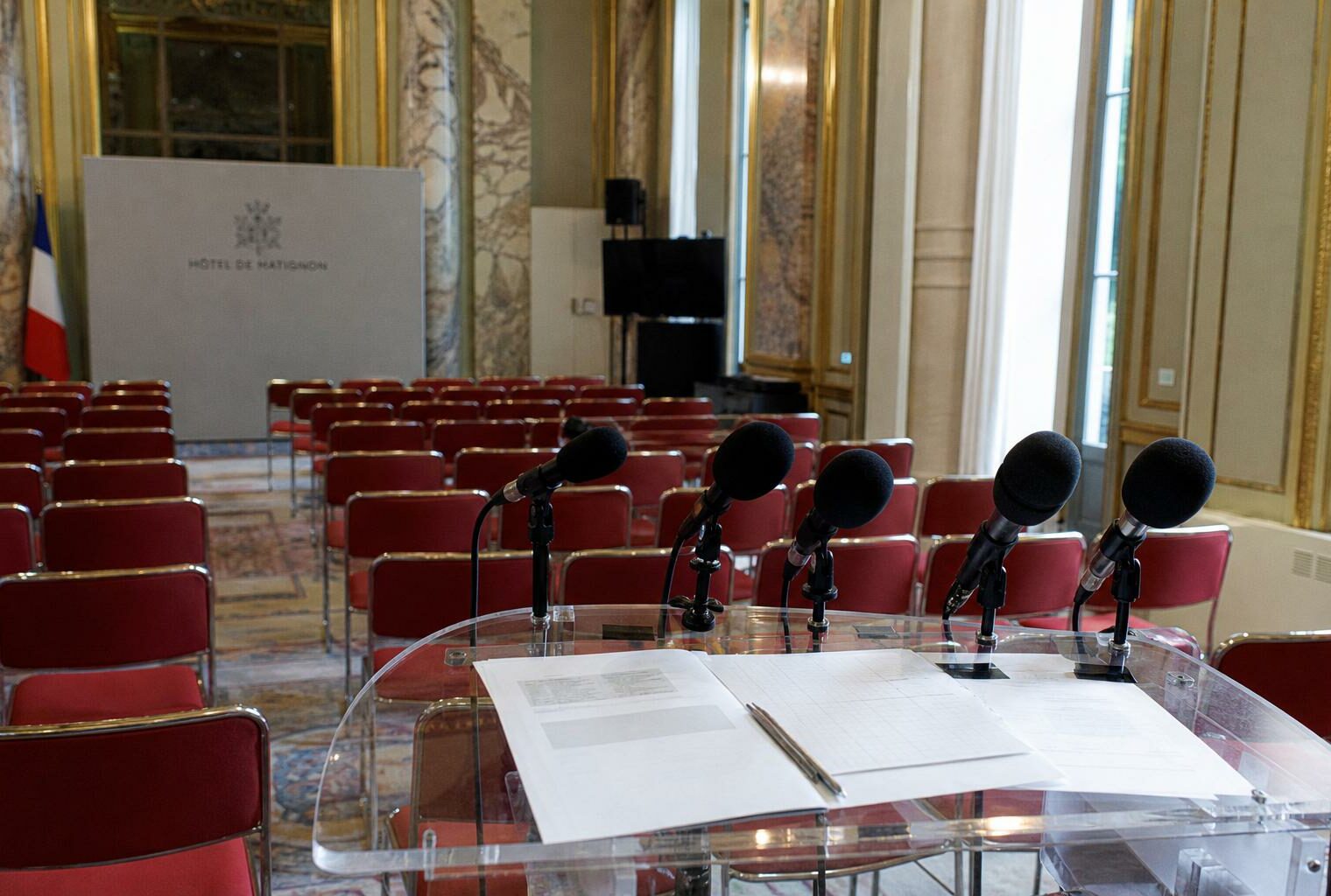 Salle de presse de Matignon vide avec pupitre, micros et sièges rouges, dans une ambiance institutionnelle française