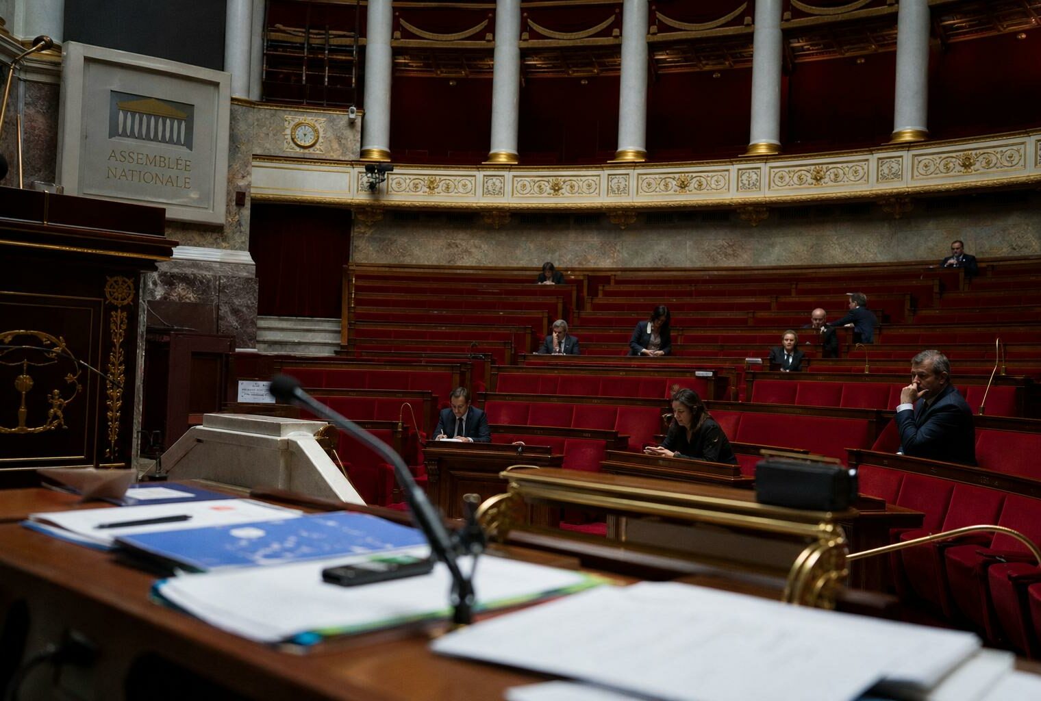 Vue documentaire de l’hémicycle de l’Assemblée nationale avec sièges rouges et micros, illustrant le débat sur l’aide à mourir.
