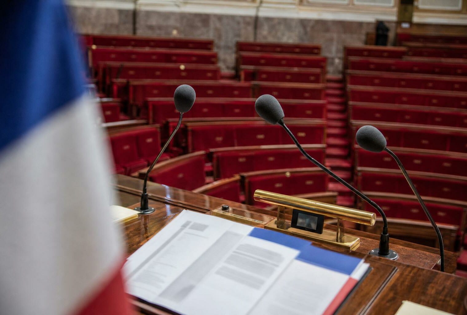 Salle de presse de l’Assemblée nationale avec pupitre vide, micros et sièges rouges, illustrant le débat sur l’aide à mourir.