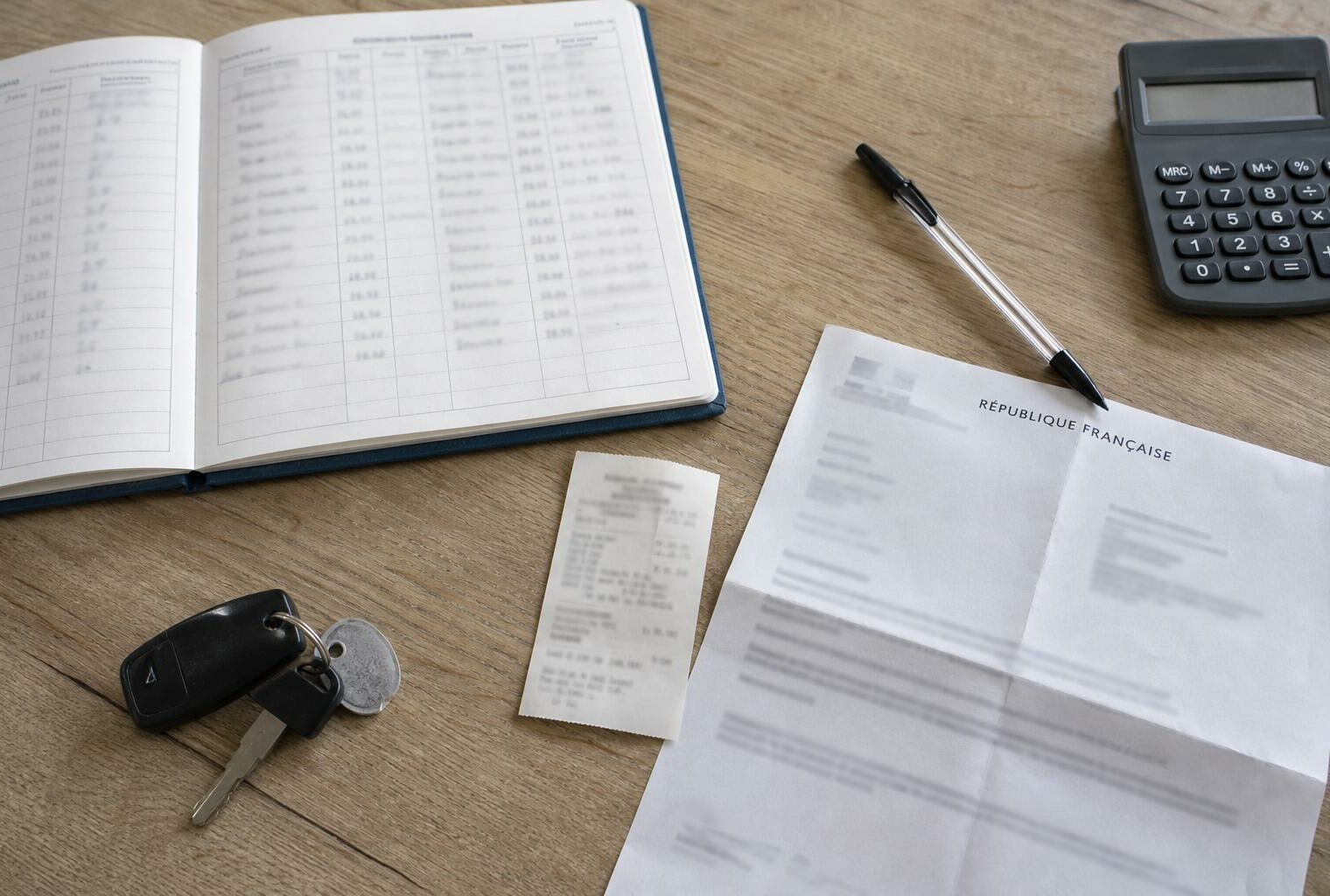 Flat lay photojournalistique d’un bureau d’aide à domicile avec carnet de trajets, reçu de carburant, calculatrice et document officiel français.