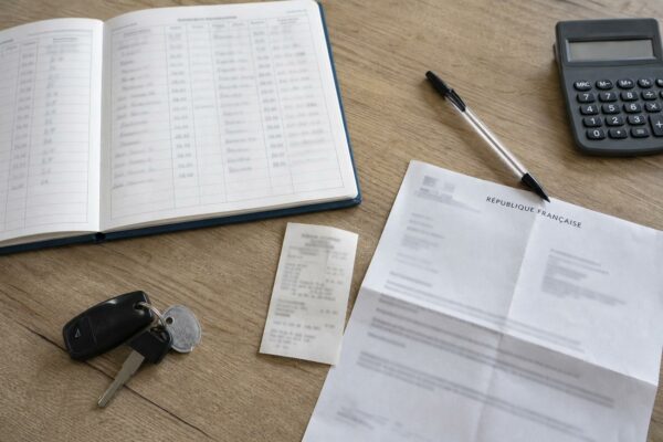 Flat lay photojournalistique d’un bureau d’aide à domicile avec carnet de trajets, reçu de carburant, calculatrice et document officiel français.