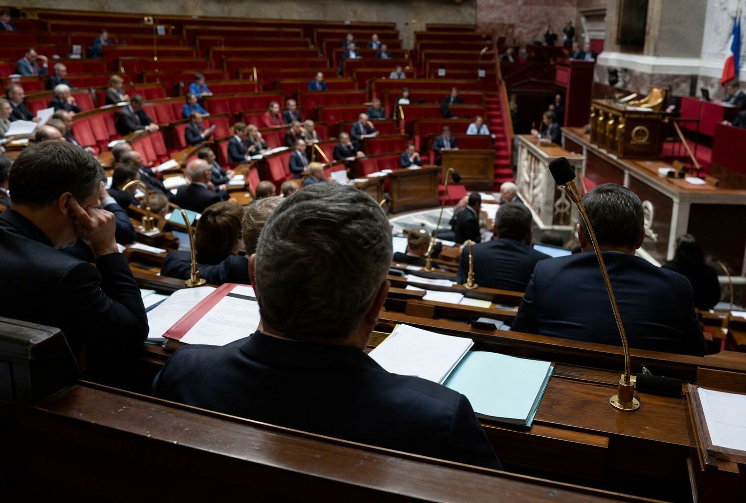 Vue large de l’hémicycle de l’Assemblée nationale pendant un vote sur le budget des armées, avec sièges rouges et pupitres visibles.
