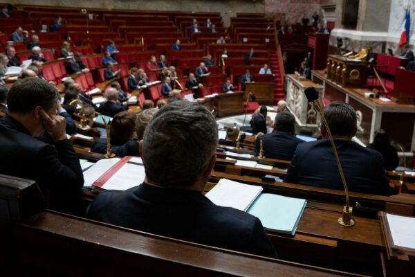 Vue large de l’hémicycle de l’Assemblée nationale pendant un vote sur le budget des armées, avec sièges rouges et pupitres visibles.