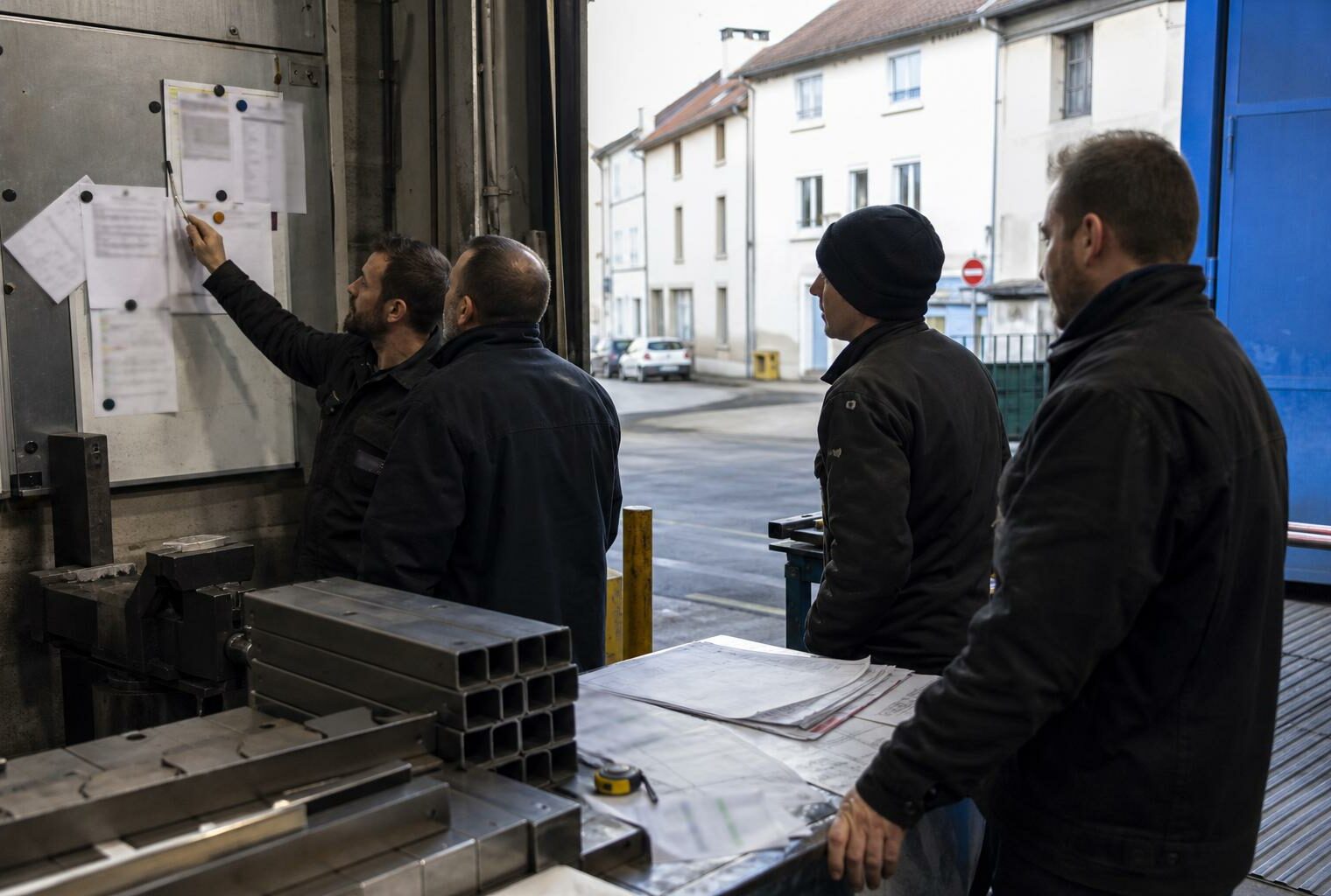Des salariés réunis dans un atelier industriel français autour d’un tableau de production flouté.