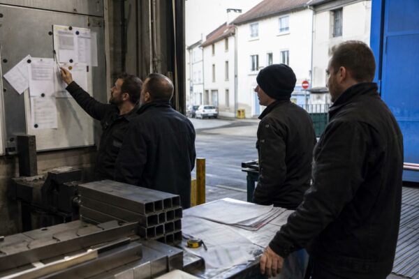 Des salariés réunis dans un atelier industriel français autour d’un tableau de production flouté.
