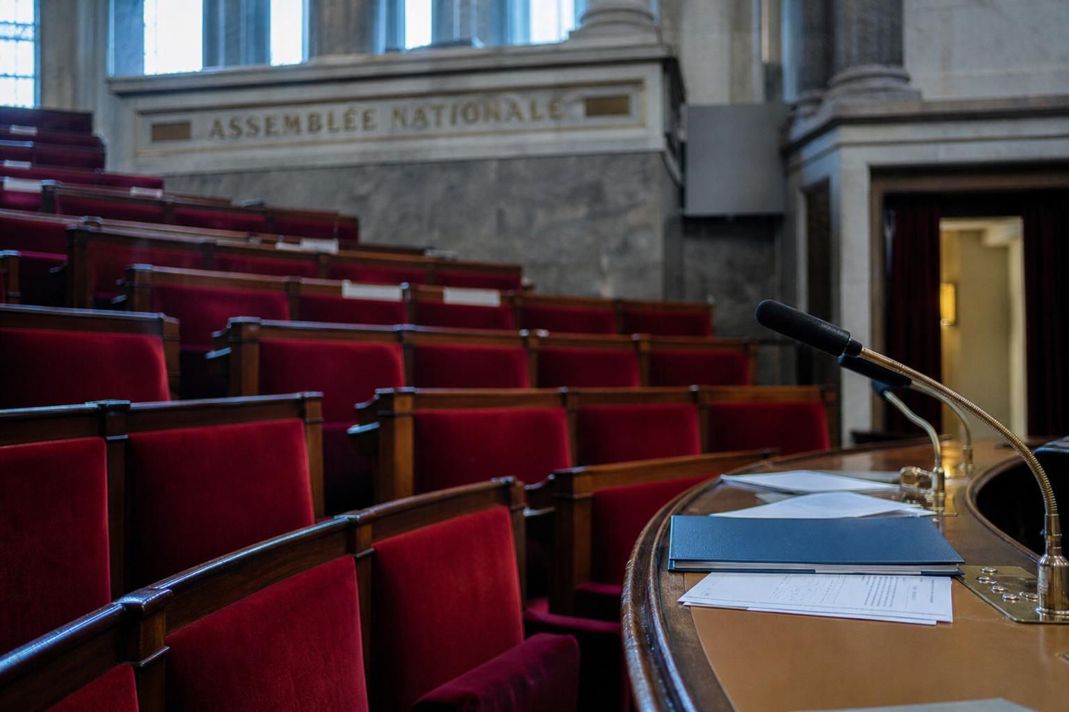 Vue oblique de l’Assemblée nationale avec sièges rouges et micros, illustrant la recomposition du centre autour de François Bayrou.