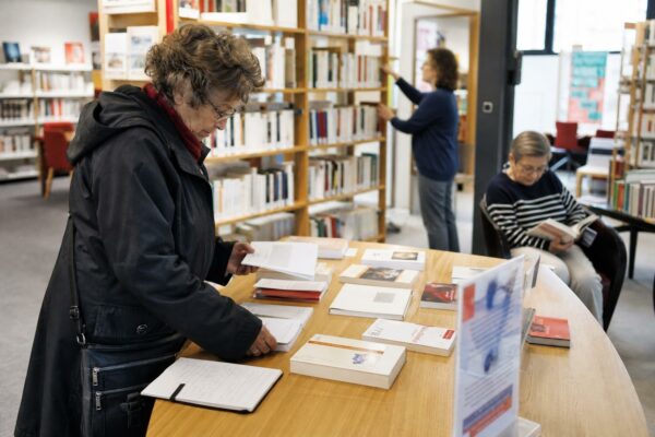 Des lecteurs anonymes consultent des livres dans une bibliothèque municipale française lumineuse