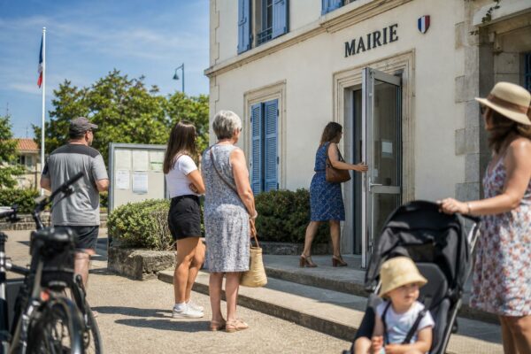 Des habitants attendent devant une mairie de province pendant une vague de chaleur précoce.