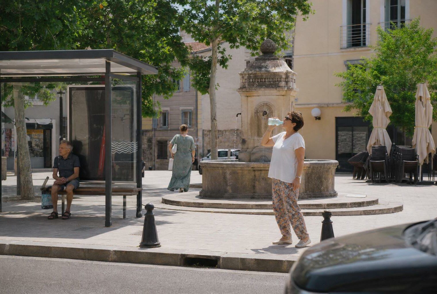 Des habitants anonymes se rafraîchissent sur une place de ville moyenne française pendant une forte chaleur