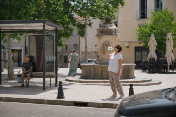 Des habitants anonymes se rafraîchissent sur une place de ville moyenne française pendant une forte chaleur