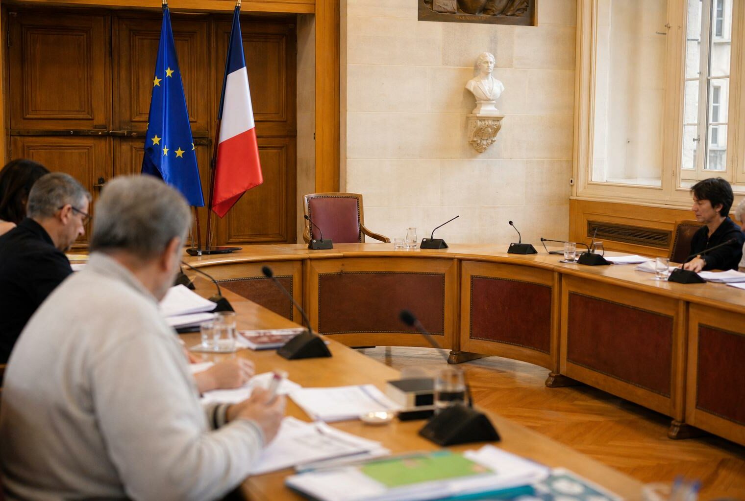 Salle municipale lumineuse avec chaise vide, micros et dossiers flous pour illustrer la préparation face à la canicule.