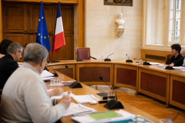 Salle municipale lumineuse avec chaise vide, micros et dossiers flous pour illustrer la préparation face à la canicule.