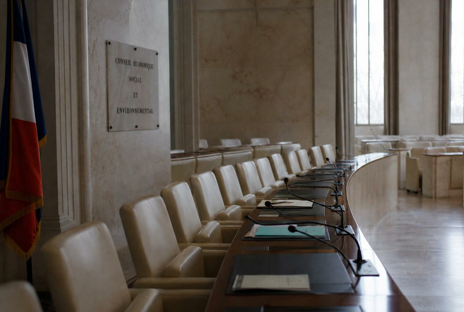 Salle institutionnelle vide du CESE au Palais d’Iéna avec sièges et micros, drapeau tricolore discret en arrière-plan