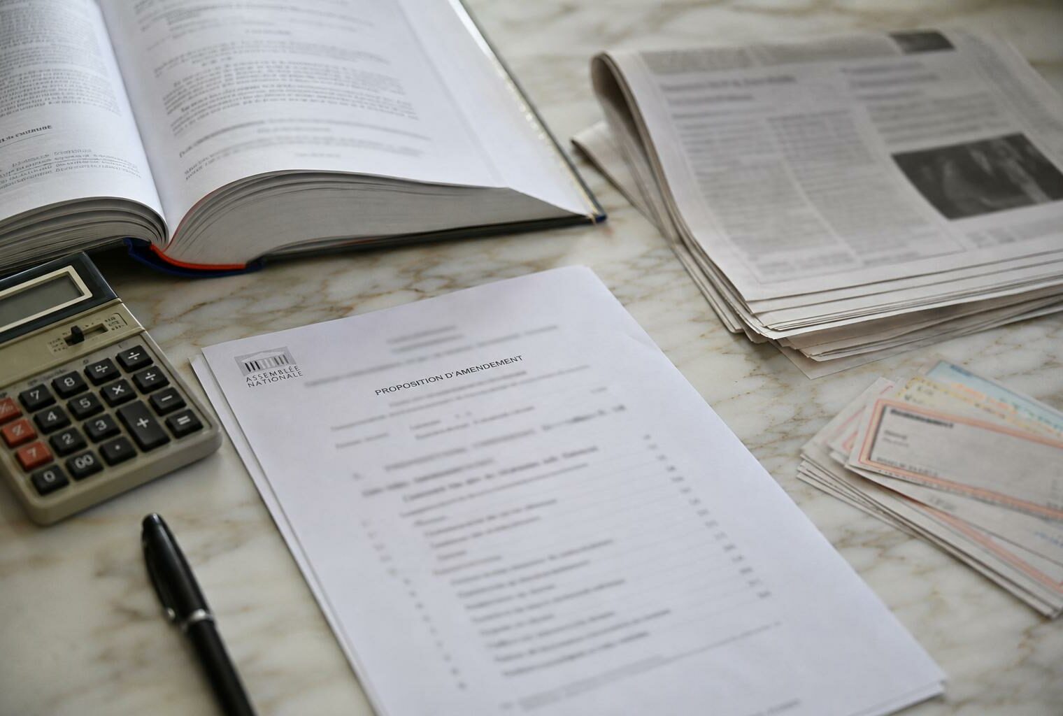 Flat lay photojournalistic of French cinema financing documents, calculator, legal code and blurred parliamentary papers on a marble desk