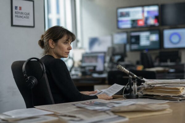 Journaliste dans une rédaction parisienne avec écrans flous et document institutionnel français en arrière-plan