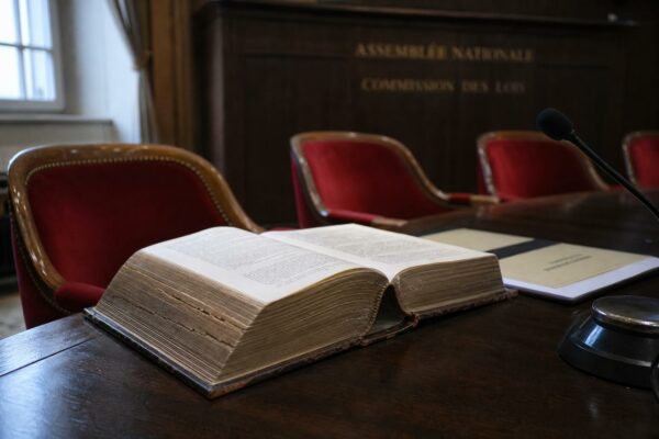 Gros plan photojournalistique d’un code juridique et d’un dossier parlementaire dans une salle de commission de l’Assemblée nationale.