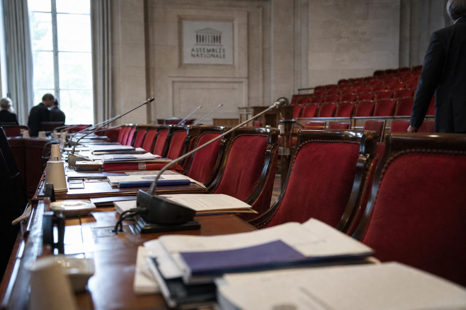 Salle de commission de l’Assemblée nationale avec micros, dossiers flous et sièges rouges, en contexte d’enquête sur le coût de l’immigration.