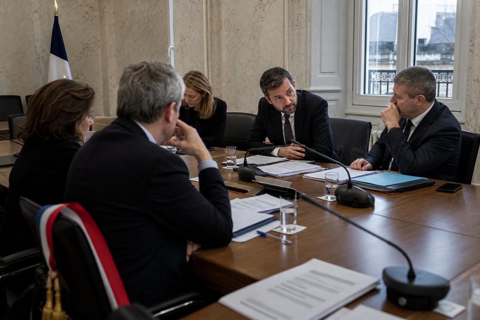 Réunion politique centriste dans une salle institutionnelle parisienne avec micros, dossiers et drapeau tricolore discret.