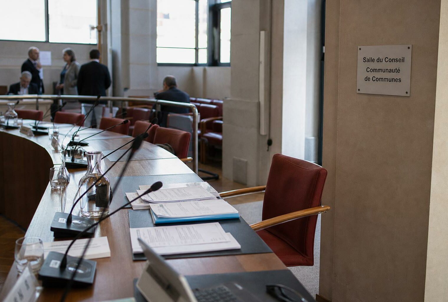 Salle de conseil communautaire française avec chaise vide, micros et dossiers flous après une démission politique.