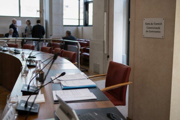 Salle de conseil communautaire française avec chaise vide, micros et dossiers flous après une démission politique.