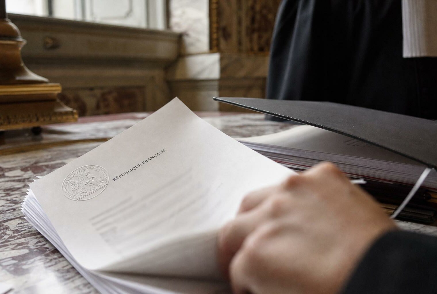 Gros plan photojournalistique sur des documents juridiques officiels français avec sceau embossé, dans un contexte institutionnel.