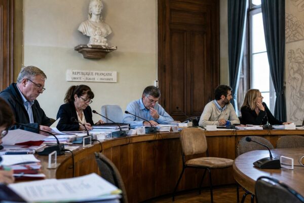 Salle municipale éclairée naturellement avec chaise vide, micros et dossiers flous pour illustrer la crise des partis politiques.