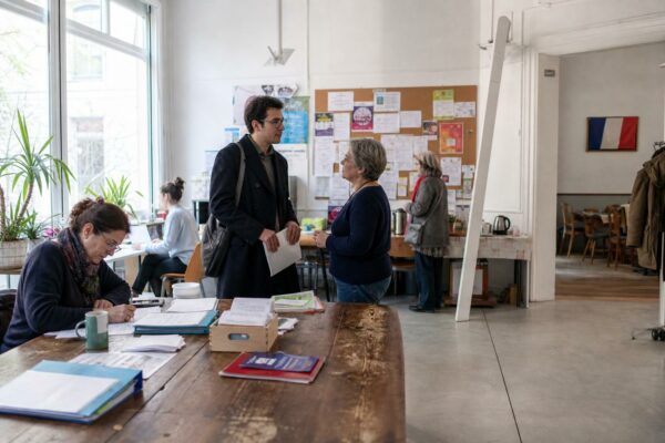 Dans une association de quartier parisienne, des anonymes échangent près d’un comptoir d’accueil lumineux.