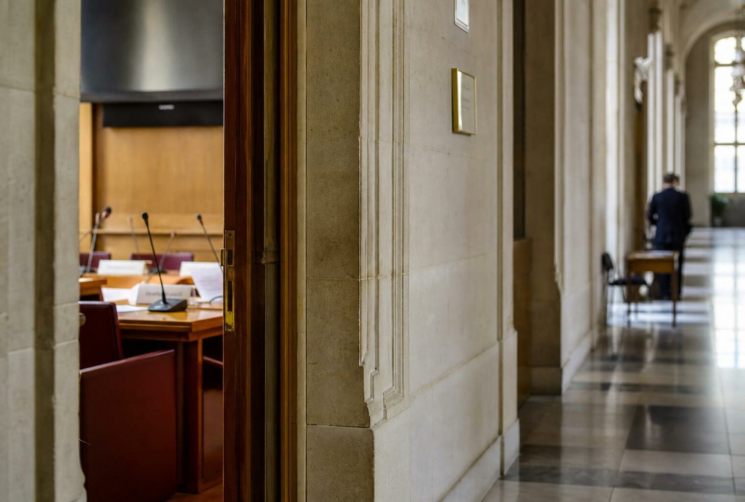 Couloir clair de l’Assemblée nationale devant une salle d’audition, ambiance institutionnelle et documentaire.