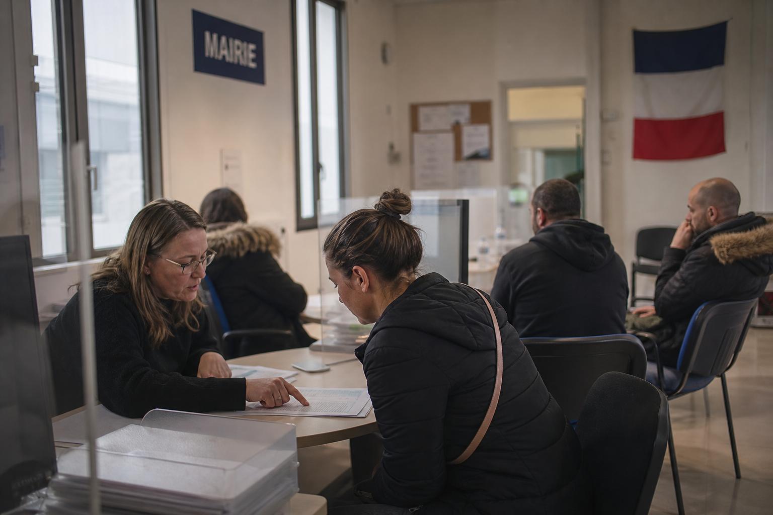 Scène de photojournalisme dans un bureau d’aide à l’emploi en France, avec des demandeurs d’emploi et un conseiller, pour illustrer le débat à gauche sur l’immigration de travail.