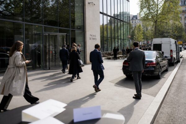 Des invités arrivent devant un immeuble parisien pour un déjeuner politique discret, dans une scène de rue claire et réaliste.