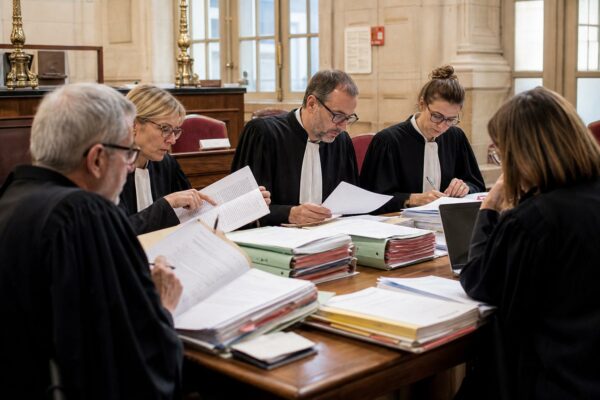 Magistrats et greffier réunis autour d’un dossier au palais de justice de Paris, dans une salle de délibéré lumineuse
