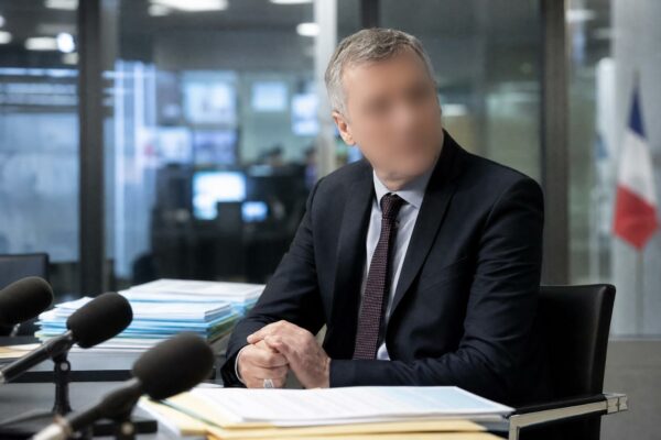 Un cadre de France Télévisions dans un bureau de rédaction, avec micros de presse et drapeau tricolore flou en arrière-plan
