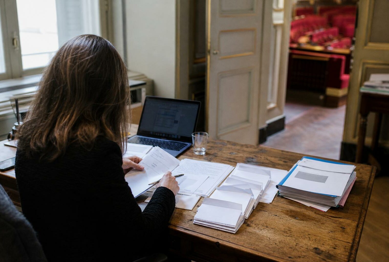 Députée dans un bureau parlementaire avec des documents de vote et les sièges rouges de l’Assemblée en arrière-plan