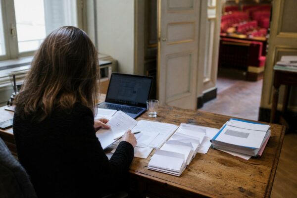 Députée dans un bureau parlementaire avec des documents de vote et les sièges rouges de l’Assemblée en arrière-plan