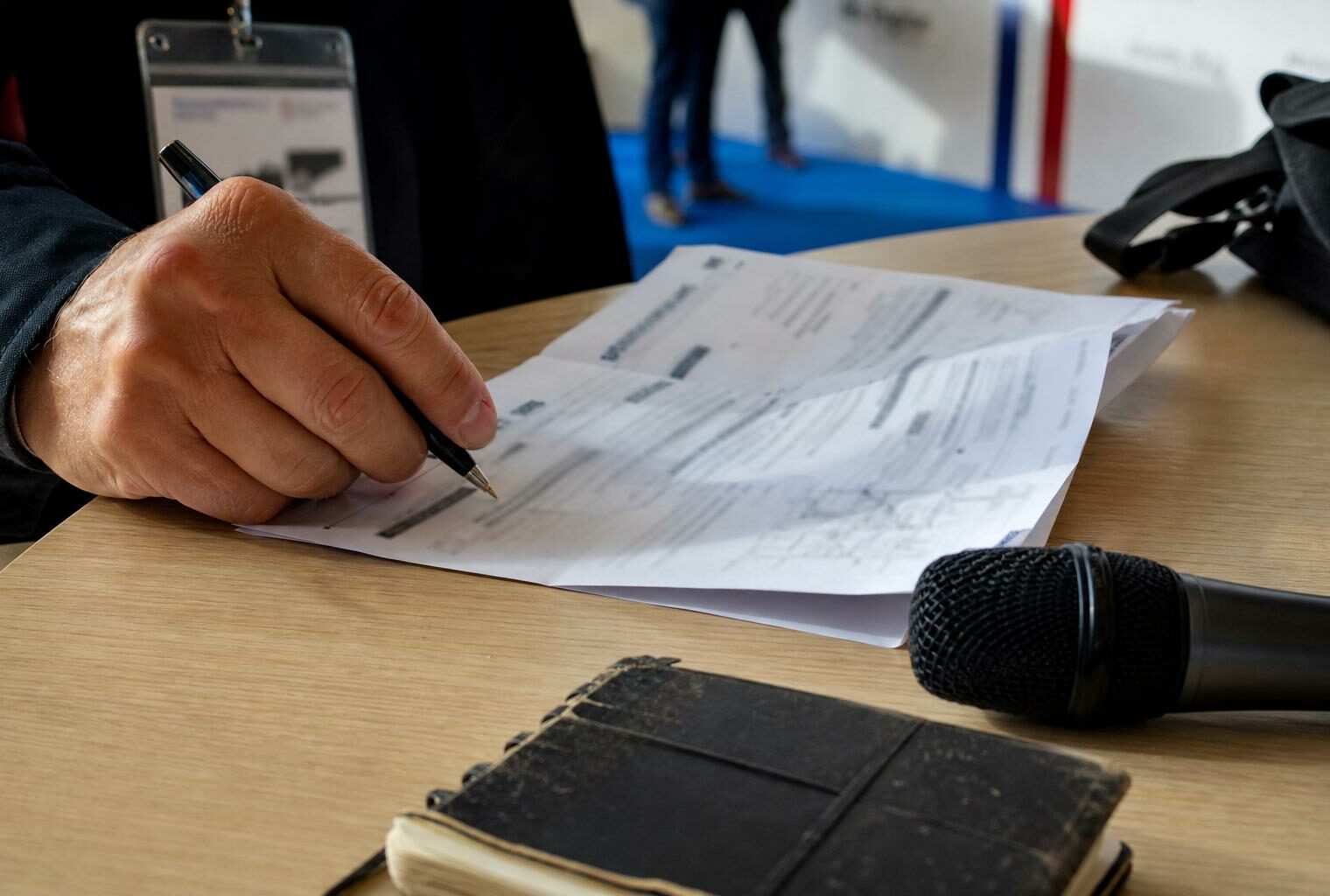Main de journaliste annotant un document près d’un micro de presse dans un hall de campagne parisien