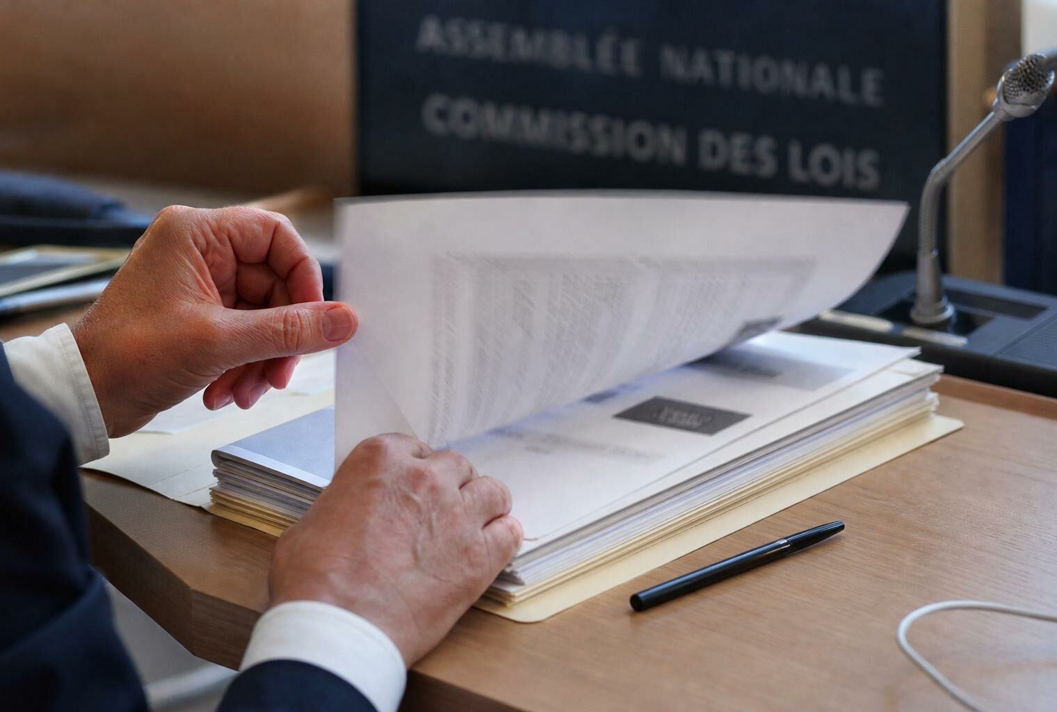 Dossier de commission avec micros et mains anonymes dans une salle d’audition parlementaire lumineuse