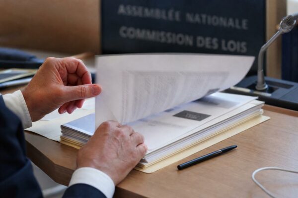 Dossier de commission avec micros et mains anonymes dans une salle d’audition parlementaire lumineuse
