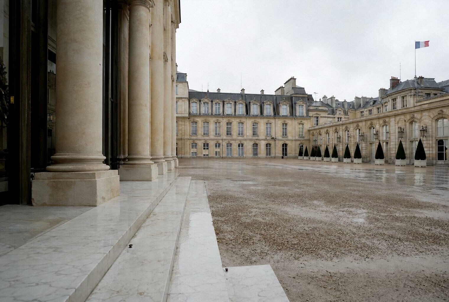 Cour intérieure de l’Élysée vide, pavés humides et drapeau tricolore discret au loin sous la lumière du jour.