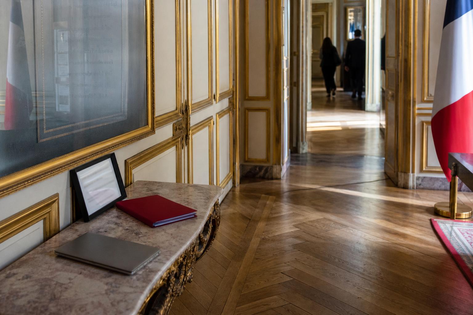 Corridor vide de l’Élysée avec lumière froide, dossier fermé et drapeau tricolore partiel, évoquant la fin de mandat d’Emmanuel Macron.