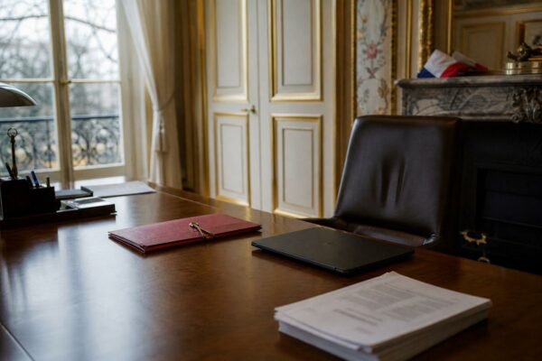 Bureau présidentiel vide à l’Élysée avec dossier fermé, documents flous et drapeau tricolore discret en arrière-plan