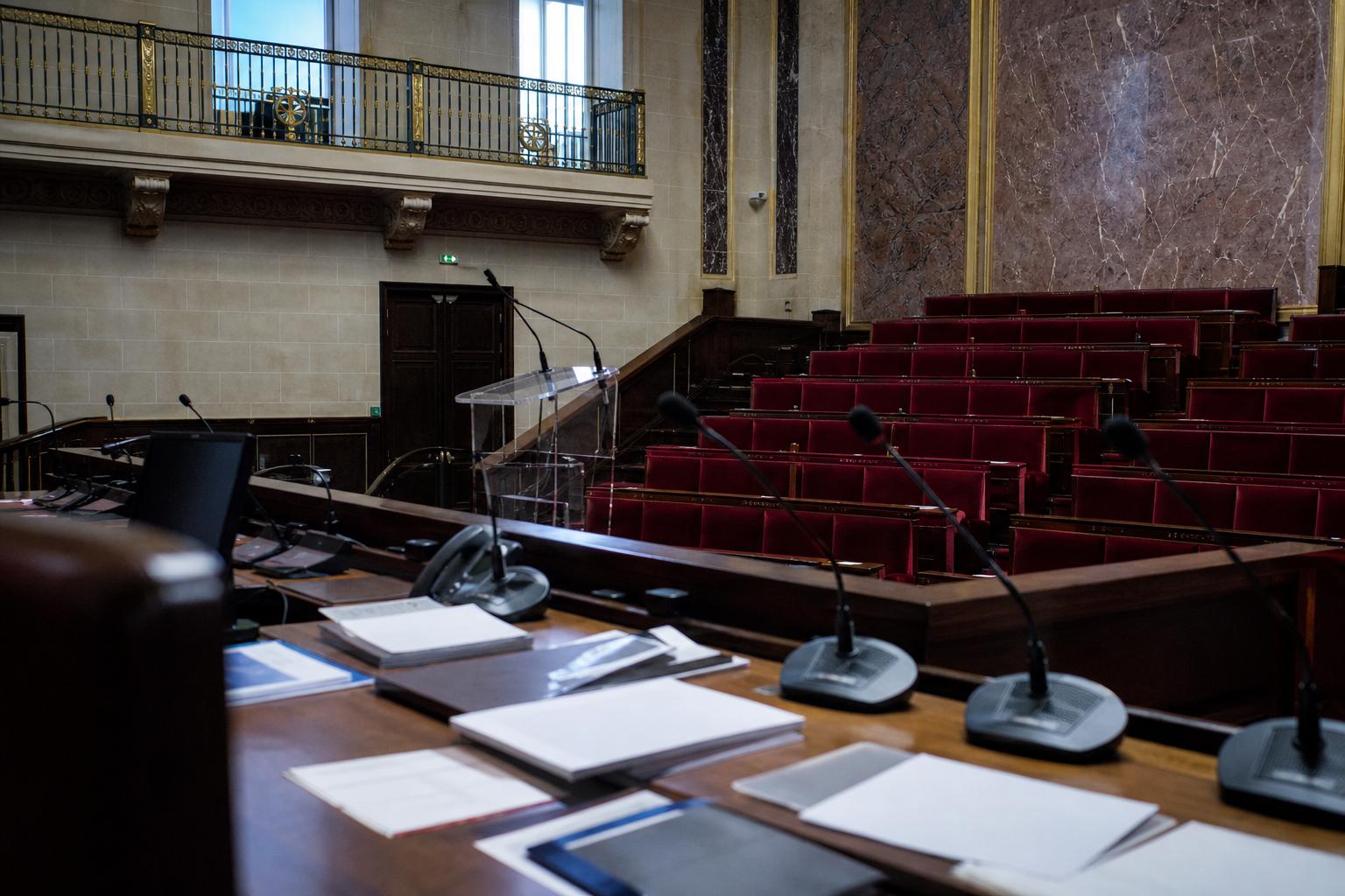 Salle de presse parlementaire vide avec micros et pupitre, ambiance institutionnelle française