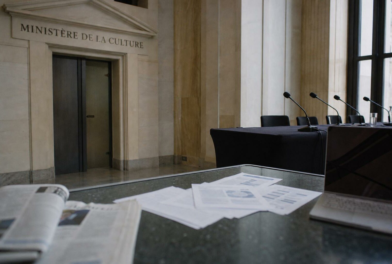 Couloir institutionnel français avec micros de presse et documents flous sur le financement du cinéma.