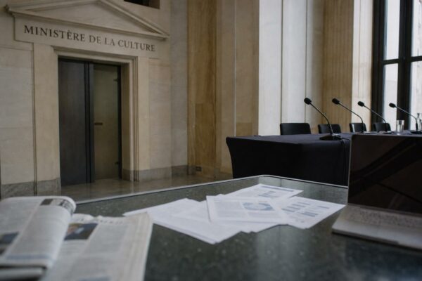 Couloir institutionnel français avec micros de presse et documents flous sur le financement du cinéma.