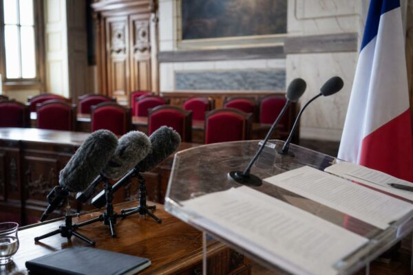 Salle de presse parlementaire française vide avec pupitre, micros et sièges rouges pour illustrer un article politique sur les carburants et les retraites