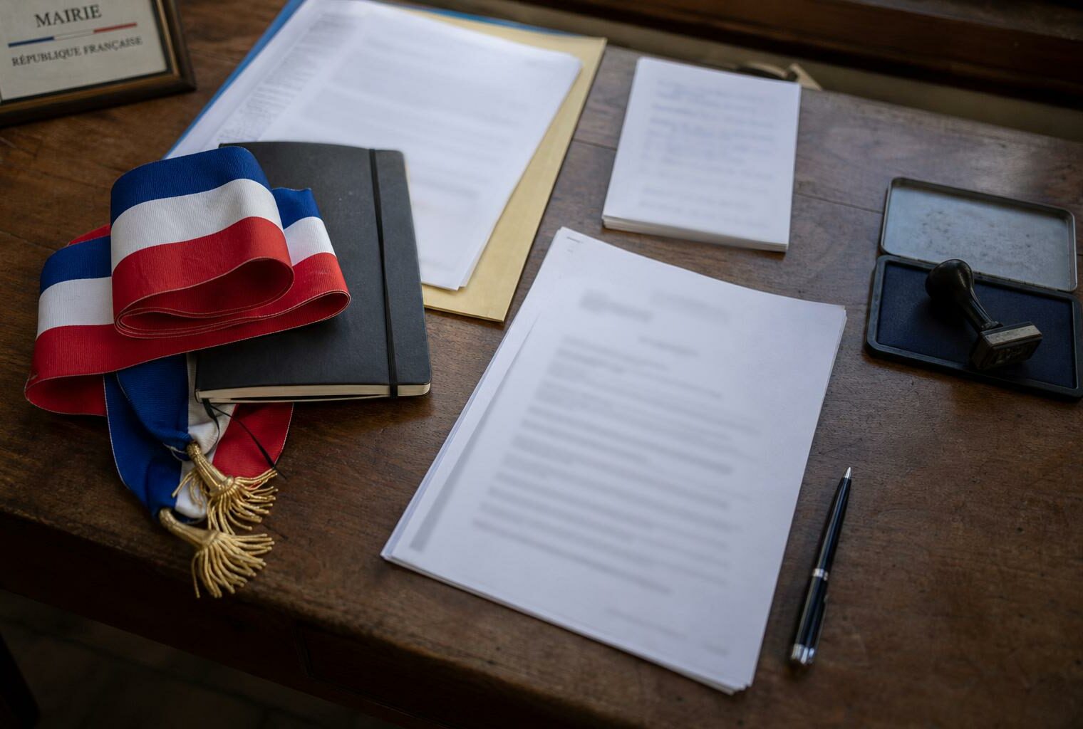 Flat lay photojournalistique sur la candidature présidentielle de Gabriel Attal avec dossier institutionnel, écharpe tricolore pliée et documents floutés sur un bureau français.