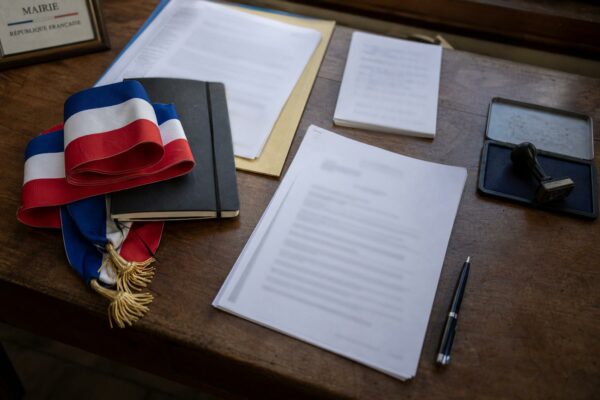 Flat lay photojournalistique sur la candidature présidentielle de Gabriel Attal avec dossier institutionnel, écharpe tricolore pliée et documents floutés sur un bureau français.
