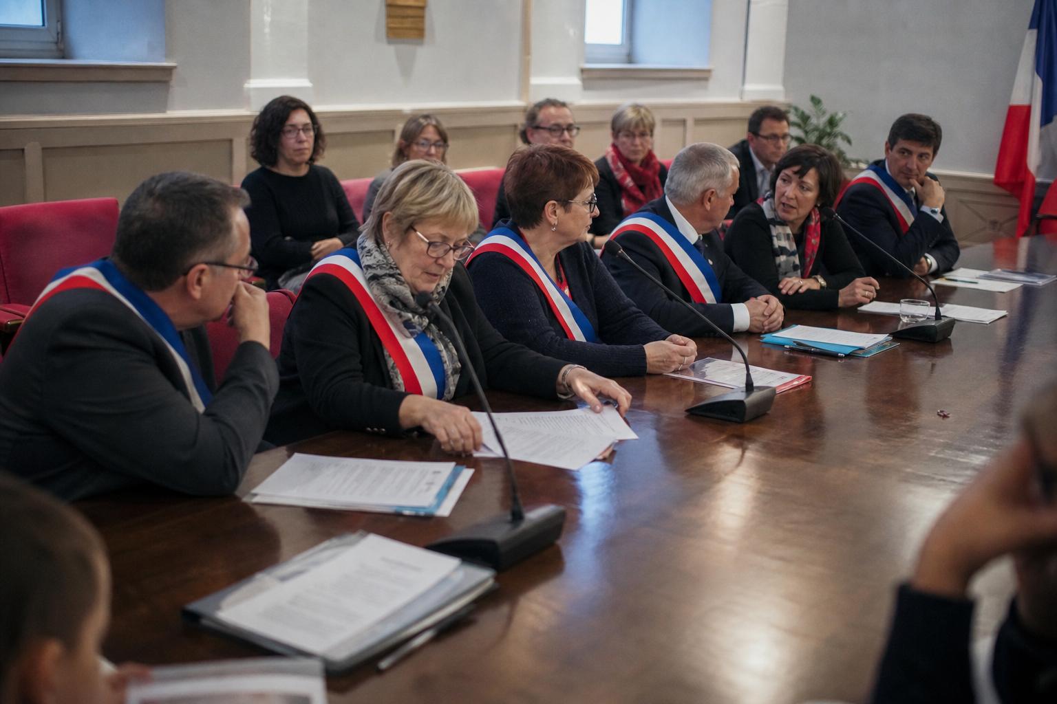 Réunion politique dans une mairie française avec des élus locaux, des micros et des documents floutés, en style photojournalisme éditorial.