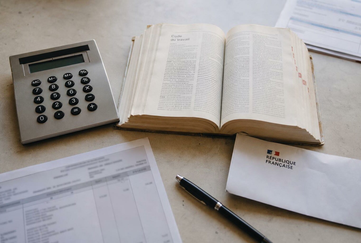 Vue en plongée d’un bureau avec calculatrice, Code du travail ouvert et document administratif français, illustrant le gel des allègements de charges face à la hausse du smic.