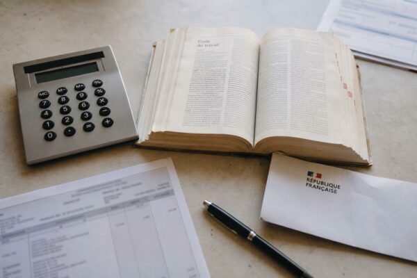 Vue en plongée d’un bureau avec calculatrice, Code du travail ouvert et document administratif français, illustrant le gel des allègements de charges face à la hausse du smic.